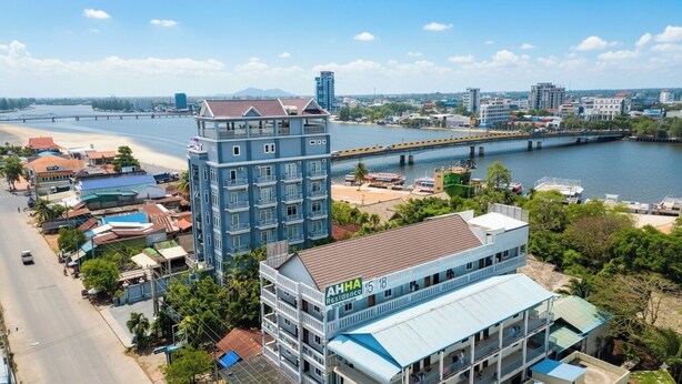 A multi-story hotel with a prominent 'AHHA Resilience' sign, situated near a river with a bridge in the background. - AHHA Residence Kampot (Kampot)