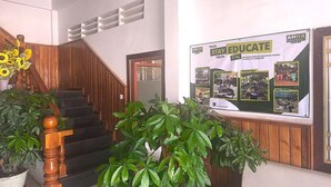 A reception area with a wooden staircase, potted plants, and a bulletin board displaying educational support information. - AHHA Residence Kampot (Kampot)