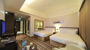 Une chambre d’hôtel avec deux lits, un bureau avec un ordinateur, une chaise, une table avec des bouteilles d’eau et un tableau au mur.