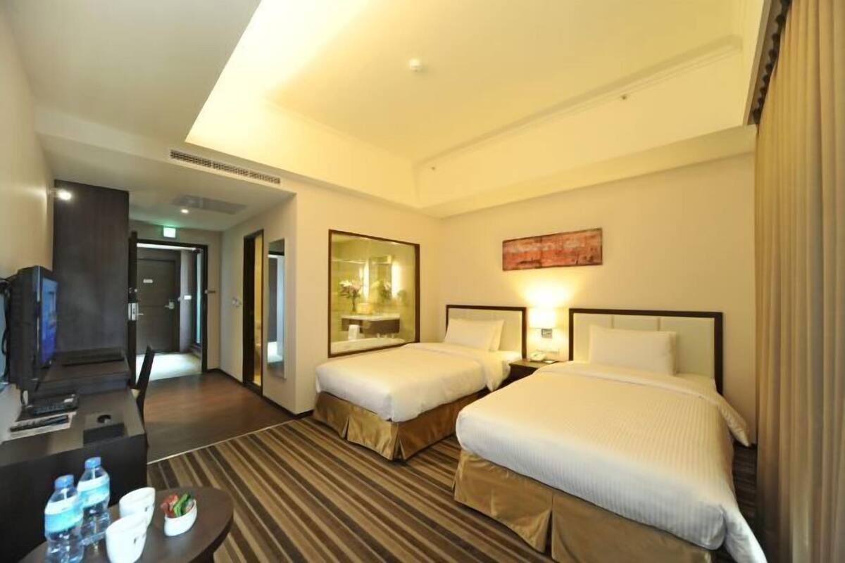 A hotel room with two beds, a desk, a TV, and a bathroom visible through an open door.