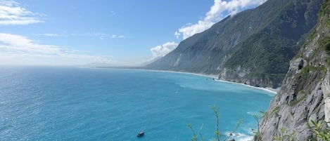 Un paysage côtier avec un ciel dégagé, une étendue d’eau et des montagnes en arrière-plan.