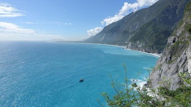 Un paysage côtier offrant une vue dégagée sur la mer, avec une falaise rocheuse et une côte lointaine.