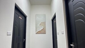 Un couloir avec deux portes sombres, dont l’une porte une plaque avec un numéro, et une œuvre d’art encadrée représentant une scène de plage, accrochée au mur.