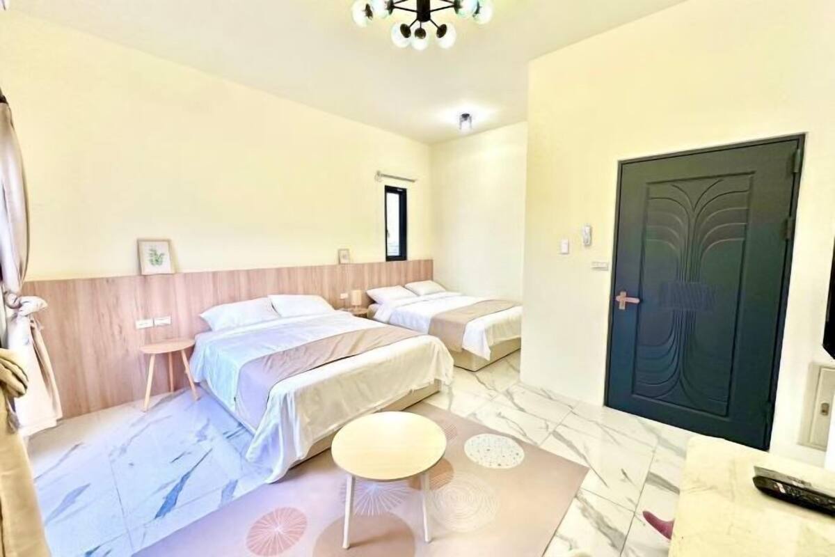 Camera d'albergo con due letti, un tavolino, una porta e una luce a soffitto.