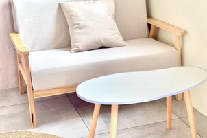 Quarto moderno com sofá em tons claros e mesa redonda com pés de madeira.