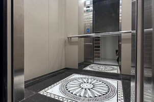 Un ascensor con interior metálico, una barandilla y un suelo con diseño geométrico.
