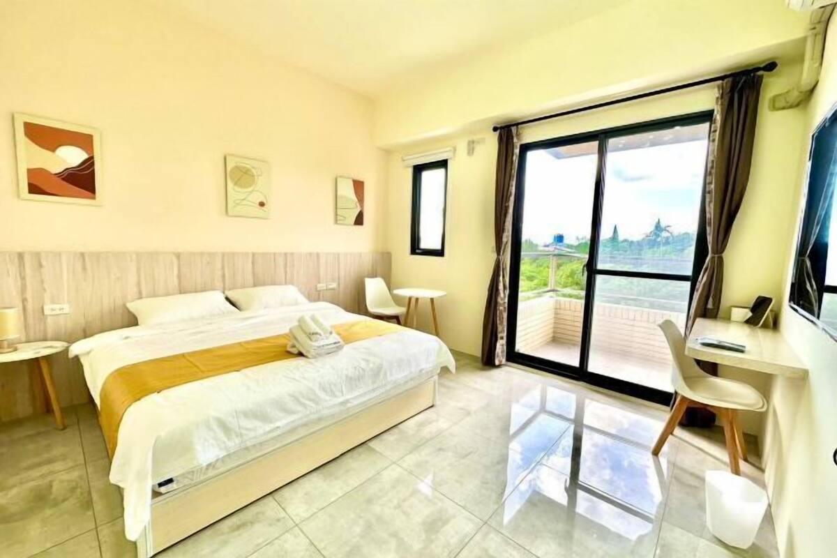 Una camera d'albergo con un letto, una scrivania, una sedia, una TV e un balcone con vista.