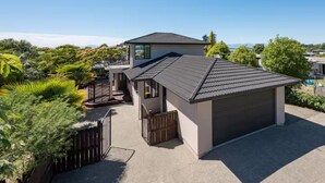 Et moderne hus med to etager og garage, omgivet af frodig vegetation og en klar blå himmel.