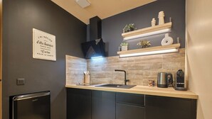 Una cocina moderna con armarios oscuros, un lavamanos de acero inoxidable y una campana extractora empotrada. Encima del lavamanos hay estantes de madera con objetos decorativos y plantas.