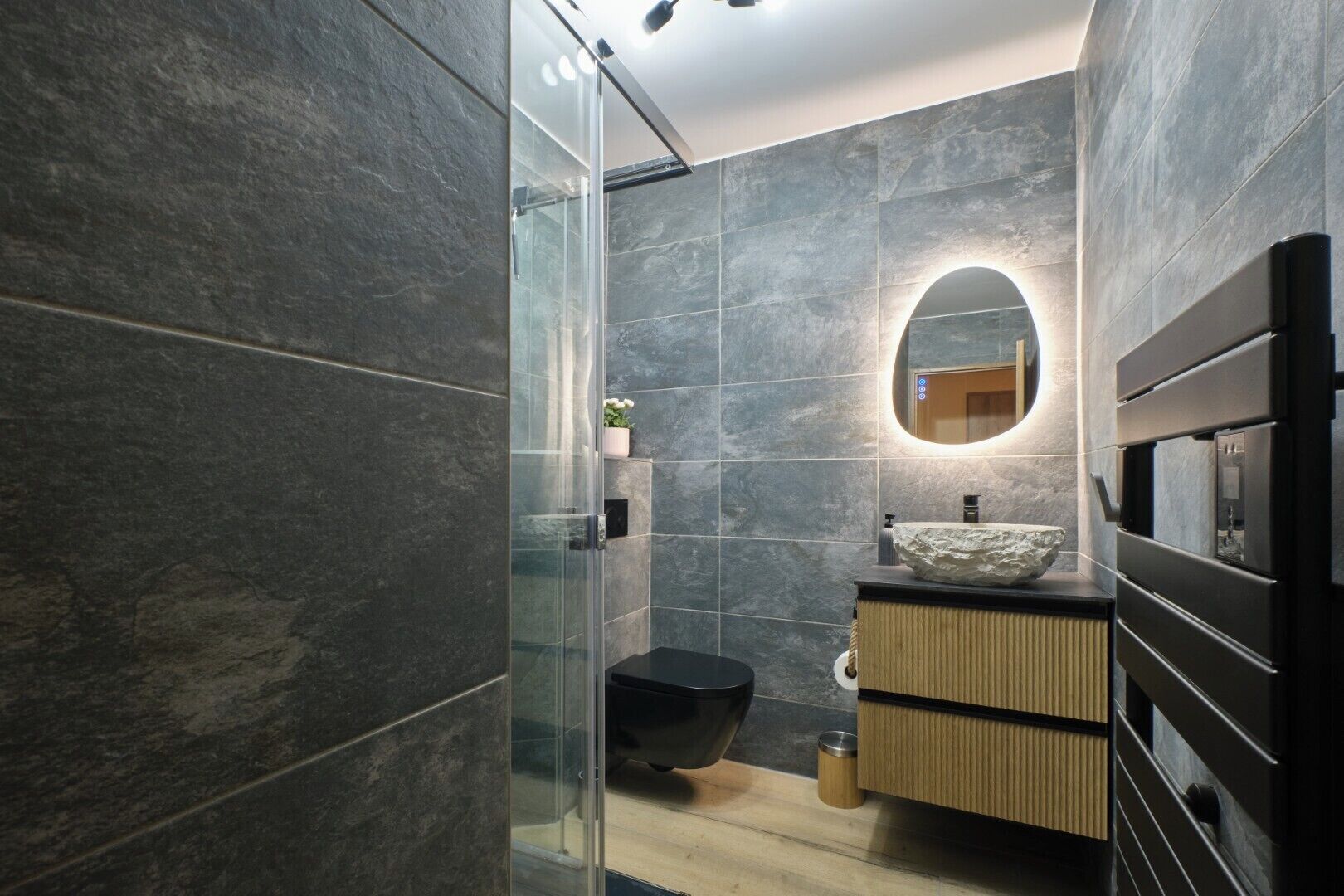 A modern bathroom with a glass shower enclosure, a sink with a stone basin, and a wooden vanity.