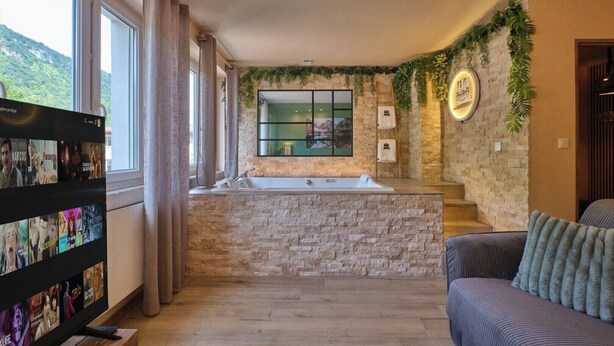 A modern bathroom with a stone wall, a large window, and a built-in bathtub. - Scandinavian Suite with private Spa & Sauna - High-end escape (Nantua)
