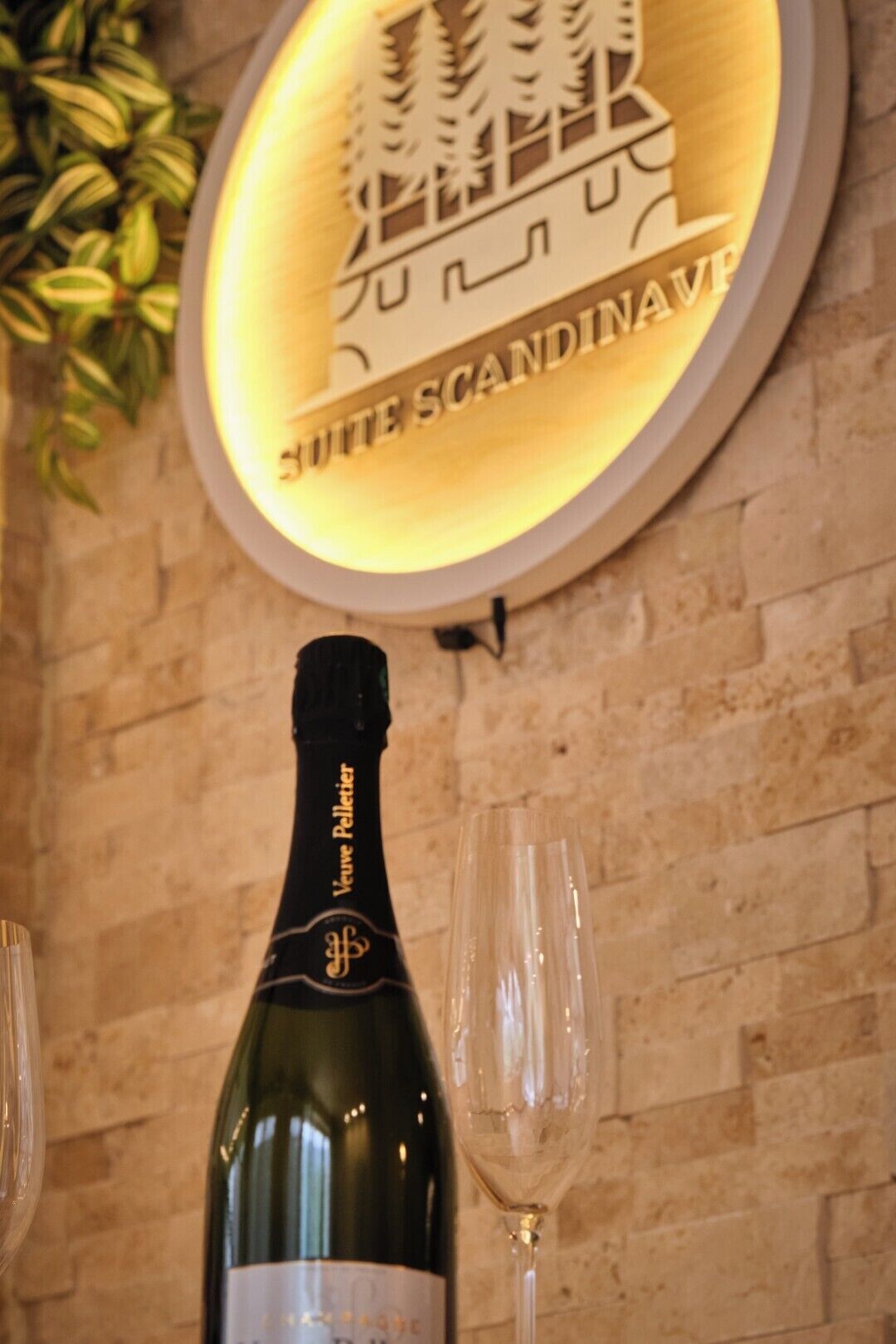 Une bouteille de champagne Veuve Clicquot et deux verres sur une table, avec une pancarte au-dessus indiquant « SUITE SCANDINAVIE ».