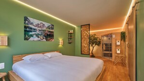 A modern hotel room with a large bed, a wooden headboard, a green accent wall, a mountain landscape painting, a wall-mounted shelf with decorative items, and a wooden door leading to a shower area. - Scandinavian Suite with private Spa & Sauna - High-end escape (Nantua)