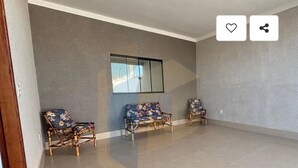 A spacious room with two wooden chairs and a sofa against a grey wall, a window, and a tiled floor. - Cozy house in Caldas Novas with private heated pool. (Caldas Novas)