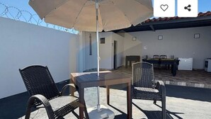 A patio with two wicker chairs, a table, and a beige umbrella. - Cozy house in Caldas Novas with private heated pool. (Caldas Novas)