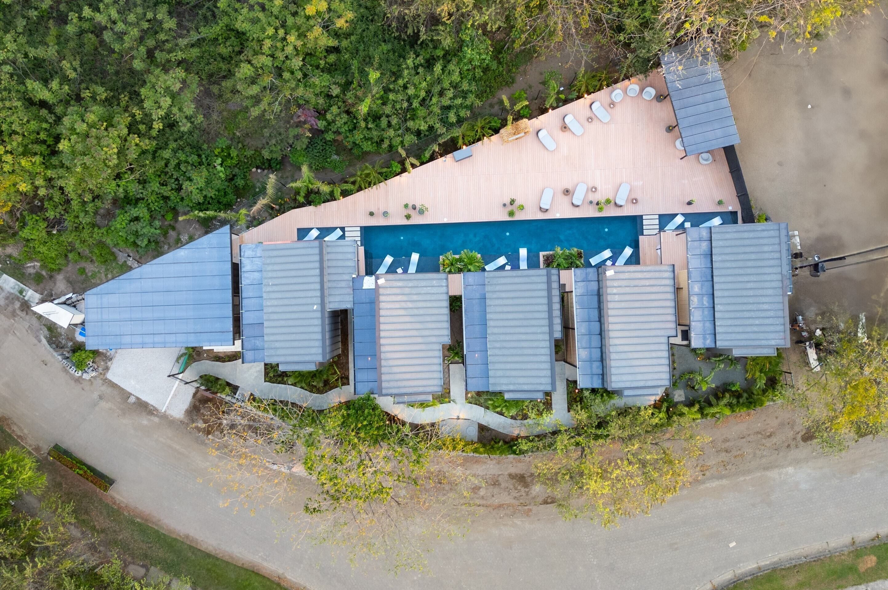 An aerial view of a hotel with a swimming pool, multiple rooms with blue roofs, and a parking area.