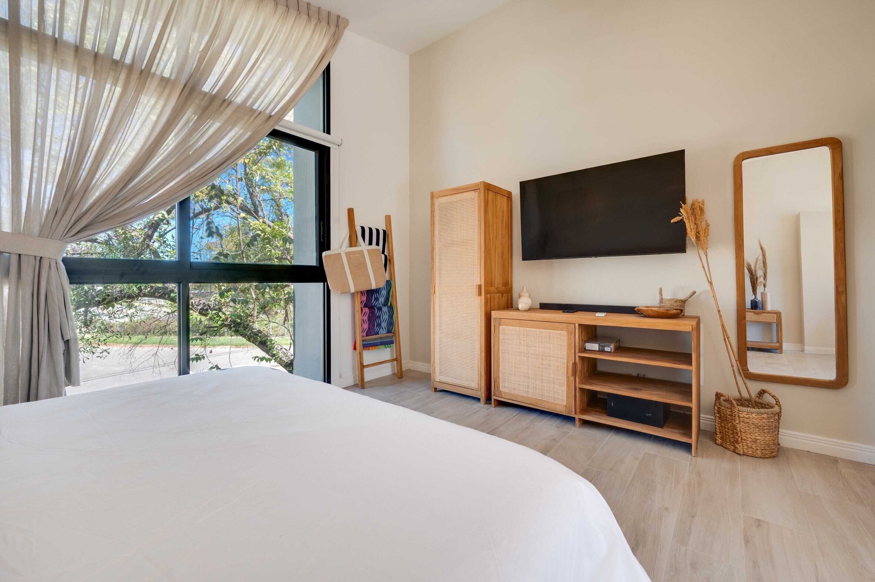 A bedroom with a large bed, a television, a wooden cabinet, and a window with curtains.