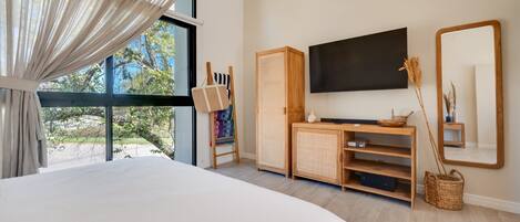 A bedroom with a large bed, a television, a wooden cabinet, and a window with curtains.