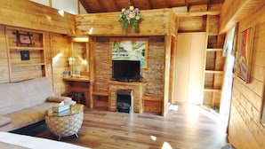 Interior de una cabaña de madera con sofá, televisión, chimenea y pared de piedra.