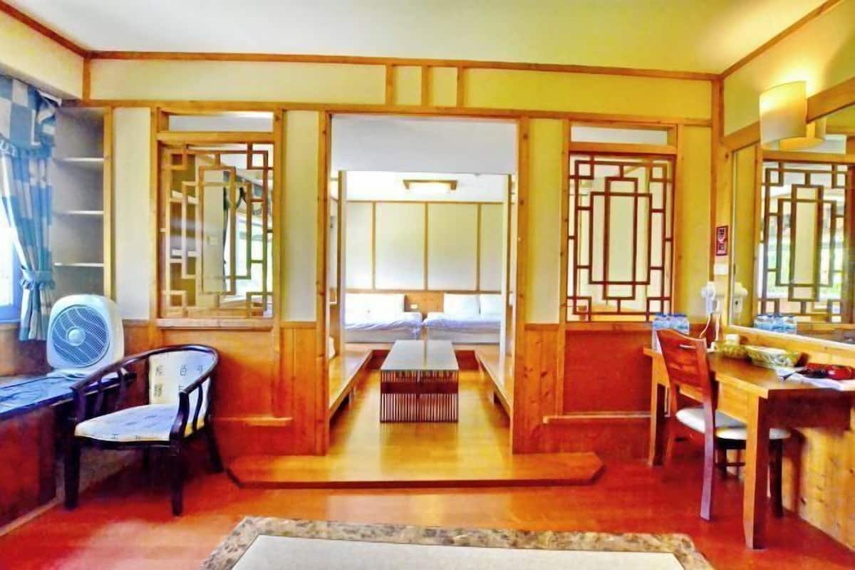 A traditional Japanese-style room with tatami flooring, a low table, a bed with a futon, and sliding doors.