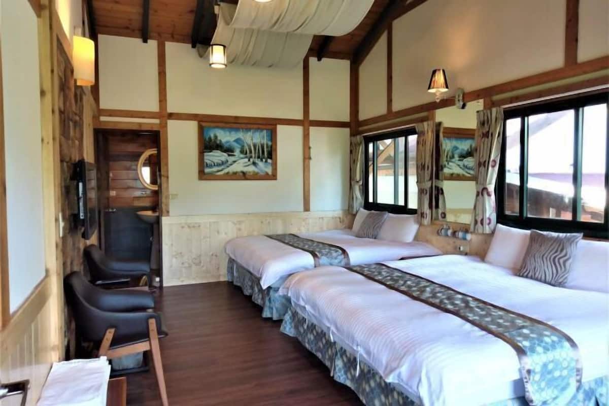 A room with a wooden ceiling, two beds with patterned bedspreads, a chair, a small table, and a painting on the wall.