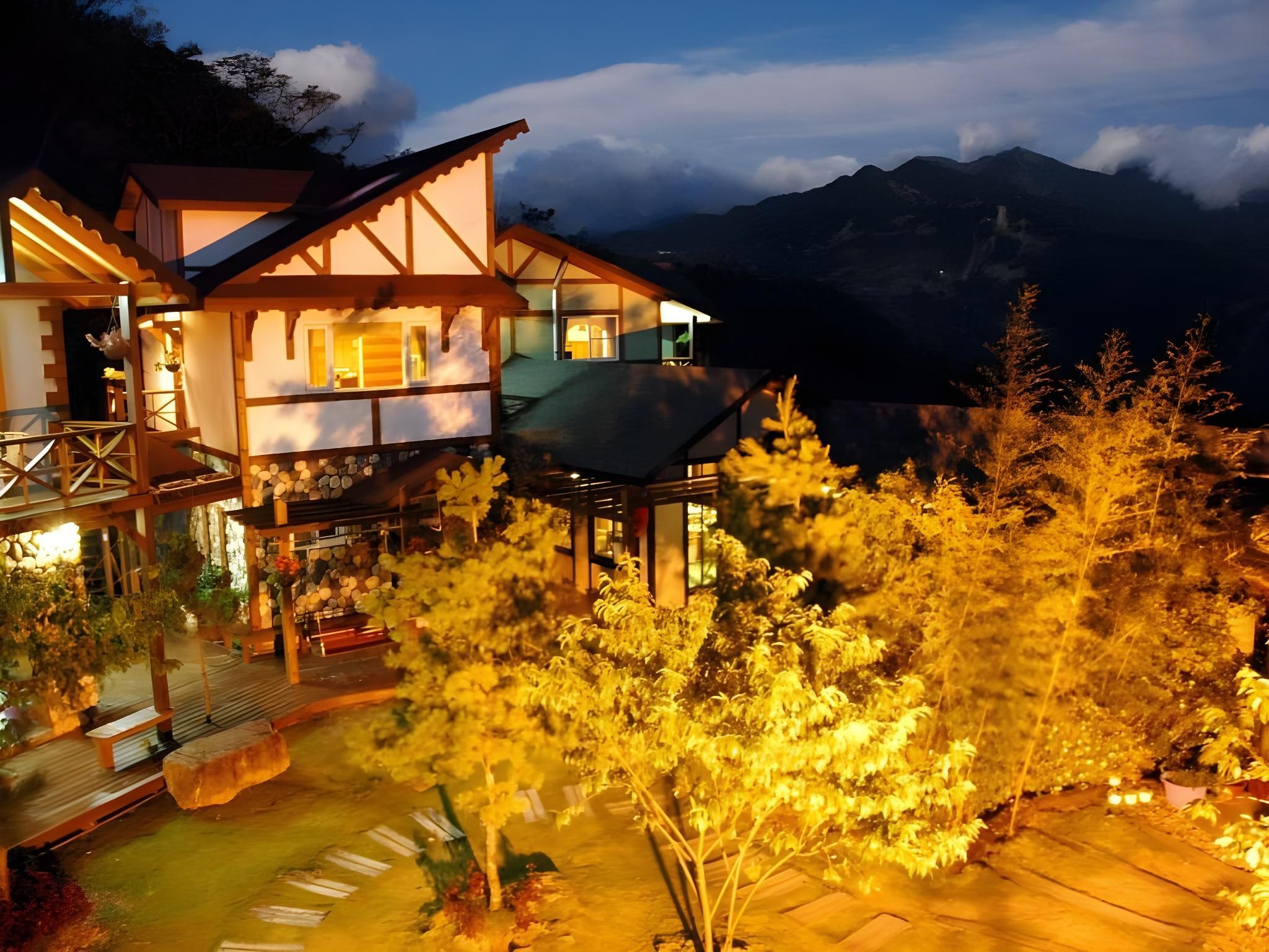 A two-story wooden building with a balcony, surrounded by trees and a mountainous backdrop.