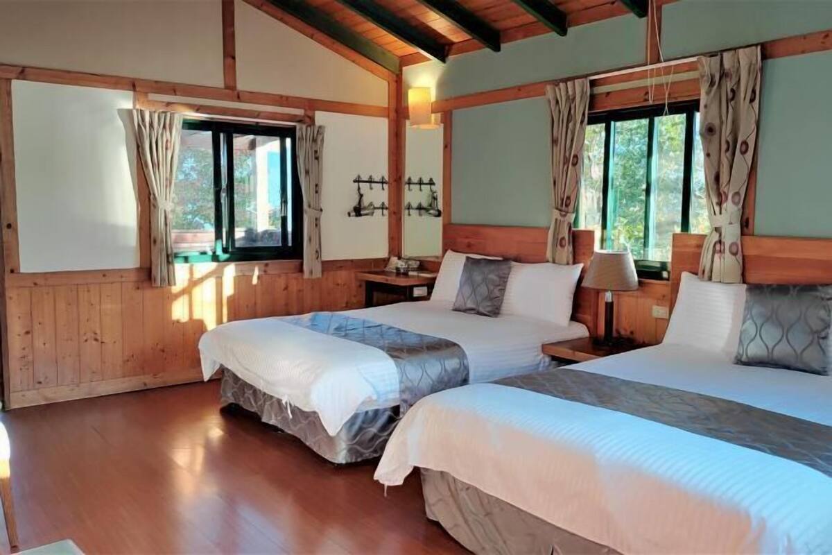 A room with two beds, wooden walls, a wooden ceiling, and a window with curtains.