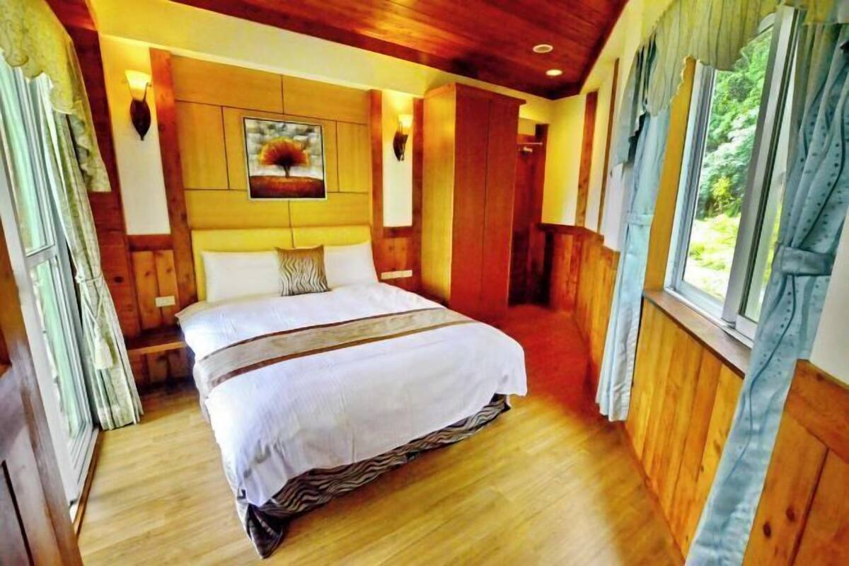 A wooden-paneled bedroom with a bed, a painting on the wall, and curtains on the windows.