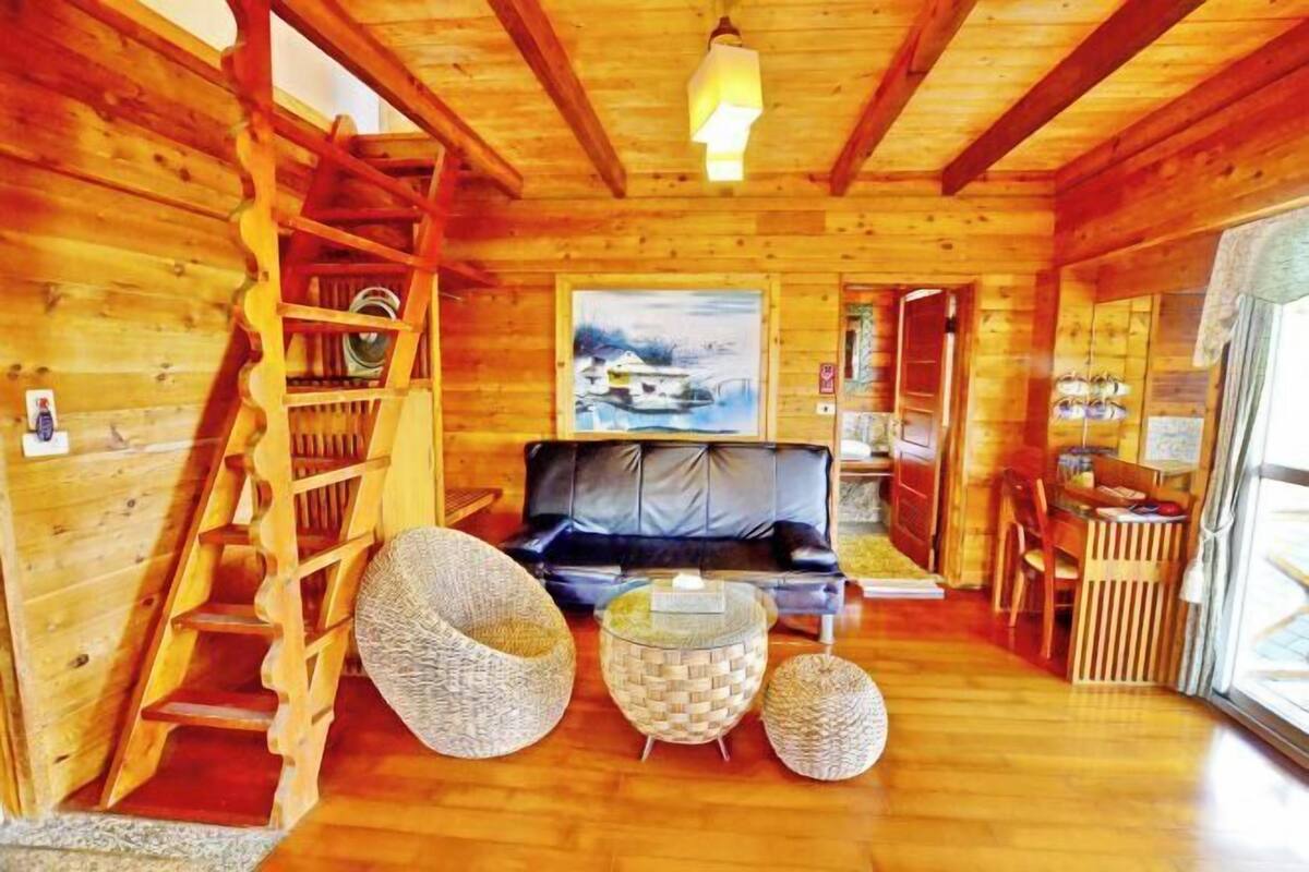A wooden interior with a sofa, two woven poufs, a ladder, and a painting on the wall.