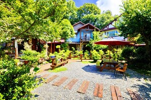 A courtyard with a gravel path, wooden benches, and tables. There are potted plants and a building with a blue facade in the background. - Shiyai Taoyuan B & B (Nantou)