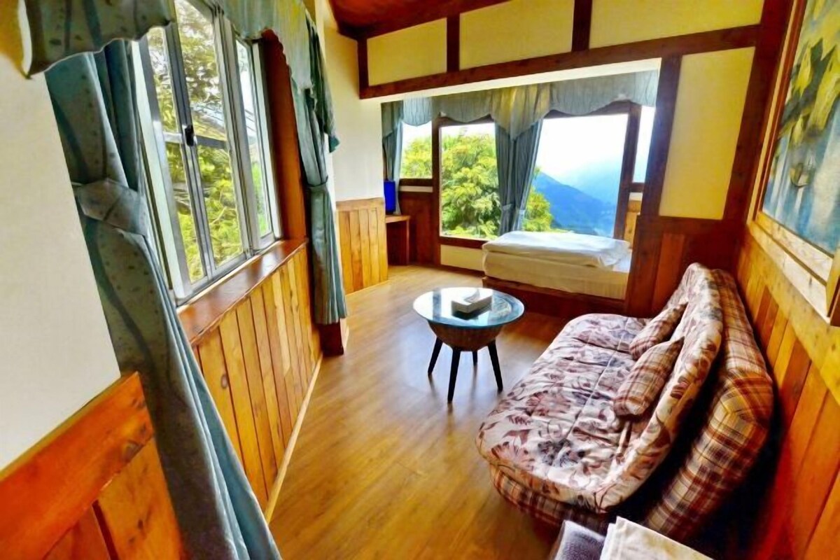 Una habitació amb sòl de fusta, un sofà, una taula petita i rodona, i finestres grans amb cortines.