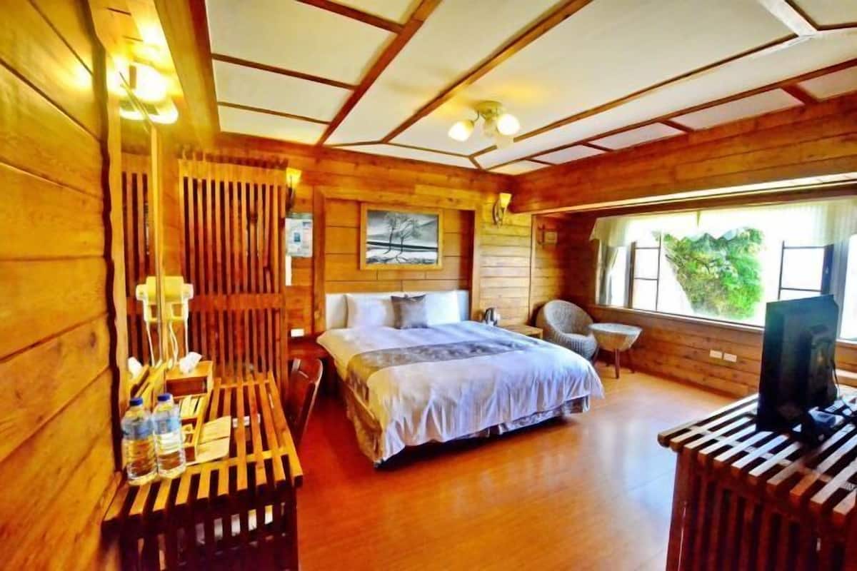A wooden cabin room with a bed, a chair, a table, and a TV.