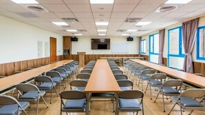 A conference room with long tables and chairs, a projector screen, and a large window with curtains. - San Chiao Hotel (Taoyuan)