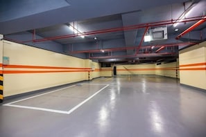 An empty parking garage with marked parking spaces, red safety railings, and visible structural beams. - San Chiao Hotel (Taoyuan)