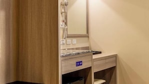 A hotel room with a wooden wardrobe, a mirror, a vanity with a sink, and a small trash bin. - San Chiao Hotel (Taoyuan)