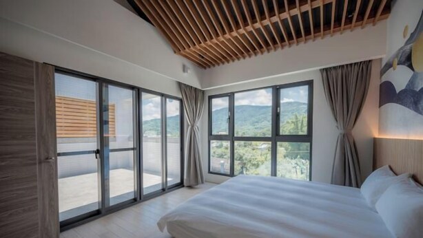 A bedroom with a large bed, sliding glass doors to a balcony, and a view of greenery. - Tiansong Villa (Yilan)