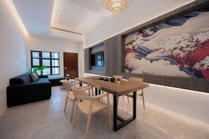 A modern living room with a dining area, featuring a large Japanese wave painting on the wall, a black sofa, and a wooden dining table with chairs.