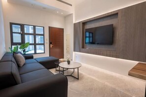 Un salon moderne avec un canapé noir, une table basse ronde et un téléviseur à écran plat fixé au mur.