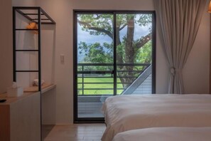 A bedroom with a bed, a desk with a lamp, and a view of a balcony with a tree. - Tiansong Villa (Yilan)