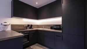 Una cucina moderna con mobili scuri, forno integrato, microonde e piano di lavoro in legno.