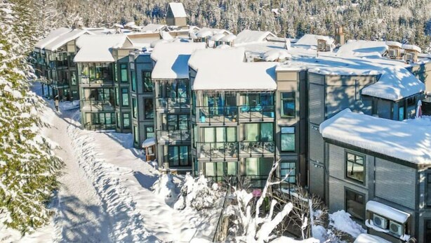 Een modern resort met meerdere gebouwen, sneeuwbedekte daken en een bergachtig achtergrond.