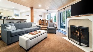 Een moderne woonkamer met een open haard, een bank, een eethoek en een keuken op de achtergrond.