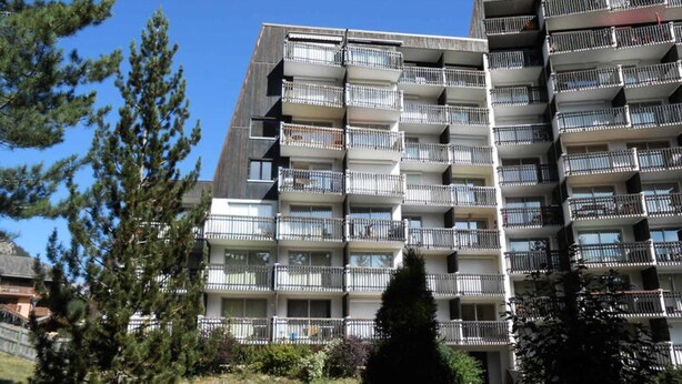 Un immeuble résidentiel à plusieurs étages, doté de balcons et entouré d’arbres.
