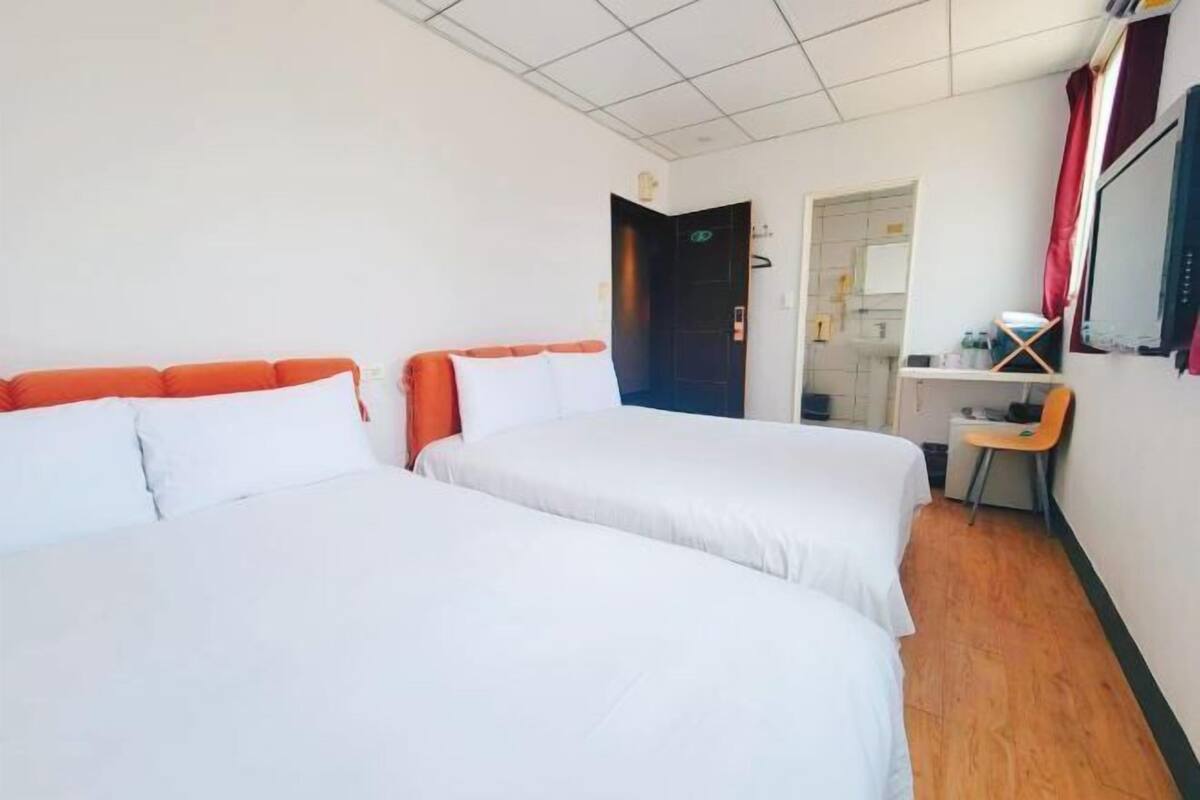 A hotel room with two beds, a desk, a chair, and a door leading to a bathroom.
