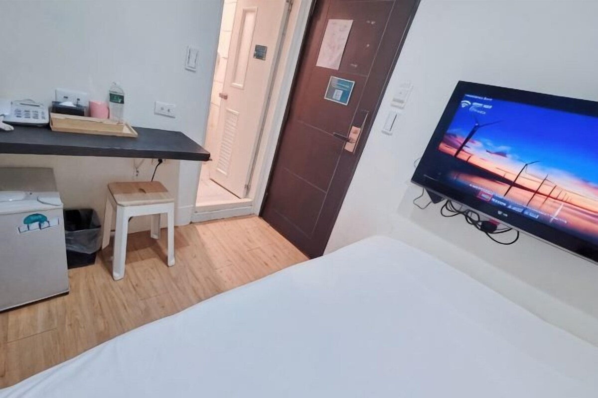 A room with a bed, a desk with a computer, a television, and a small stool.
