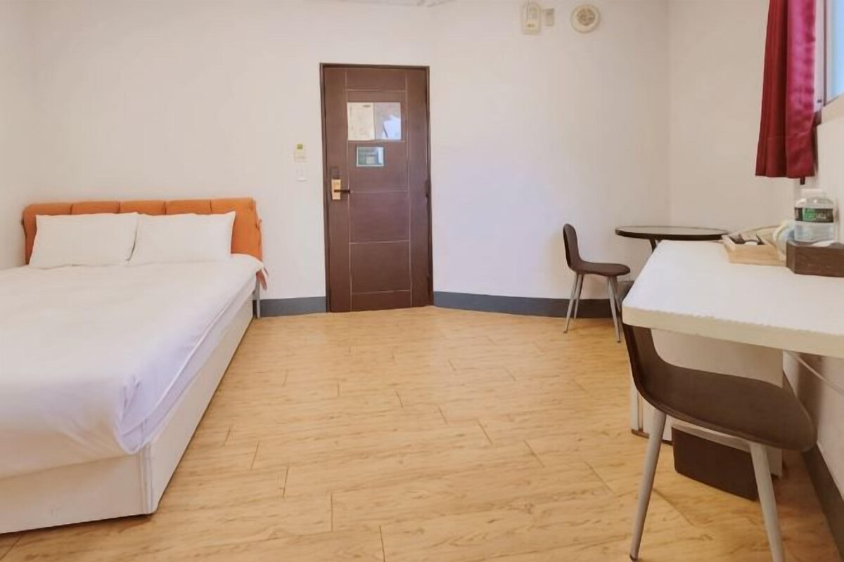 A room with a bed, a desk, a chair, and a door.
