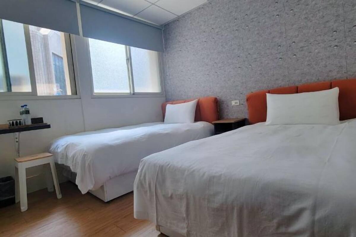 A hotel room with two beds, a small desk, and a window.