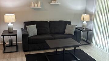 A modern living room with a black sofa, two side tables with lamps, a coffee table, and decorative shelves.
