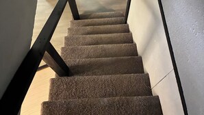 Un escalier dont les marches sont recouvertes de moquette, menant à un palier.