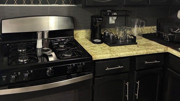 Une cuisine avec des meubles de couleur noire, une cuisinière en acier inoxydable et un dosseret décoré.